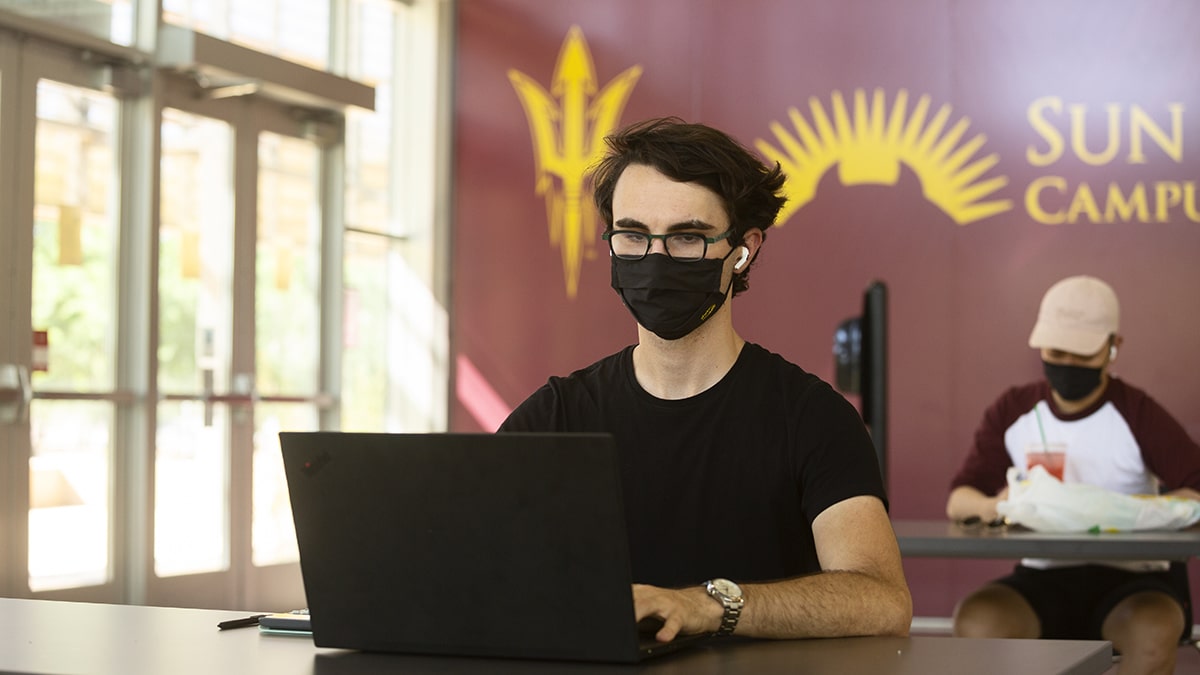 Student in classroom with laptop and face covering