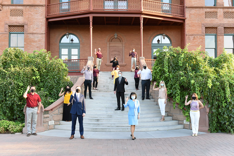 Members of the ASU Leadership Institute stand, socially distanced, on the steps of Old Main. They are wearing face masks and holding their hands in the ASU pitchfork.