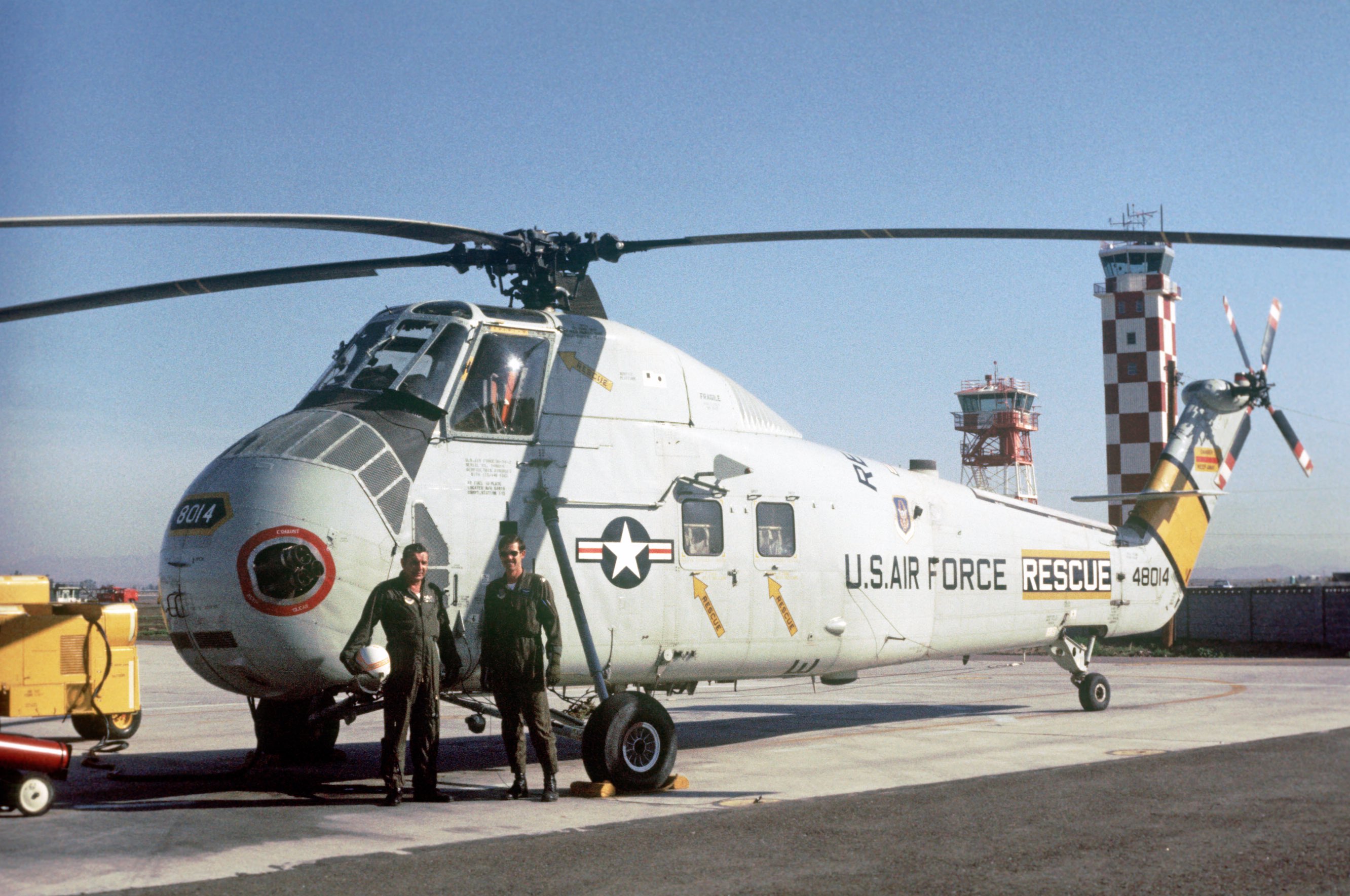 Two men standing in front of a HH-3E Jolly Green Giant helicopter