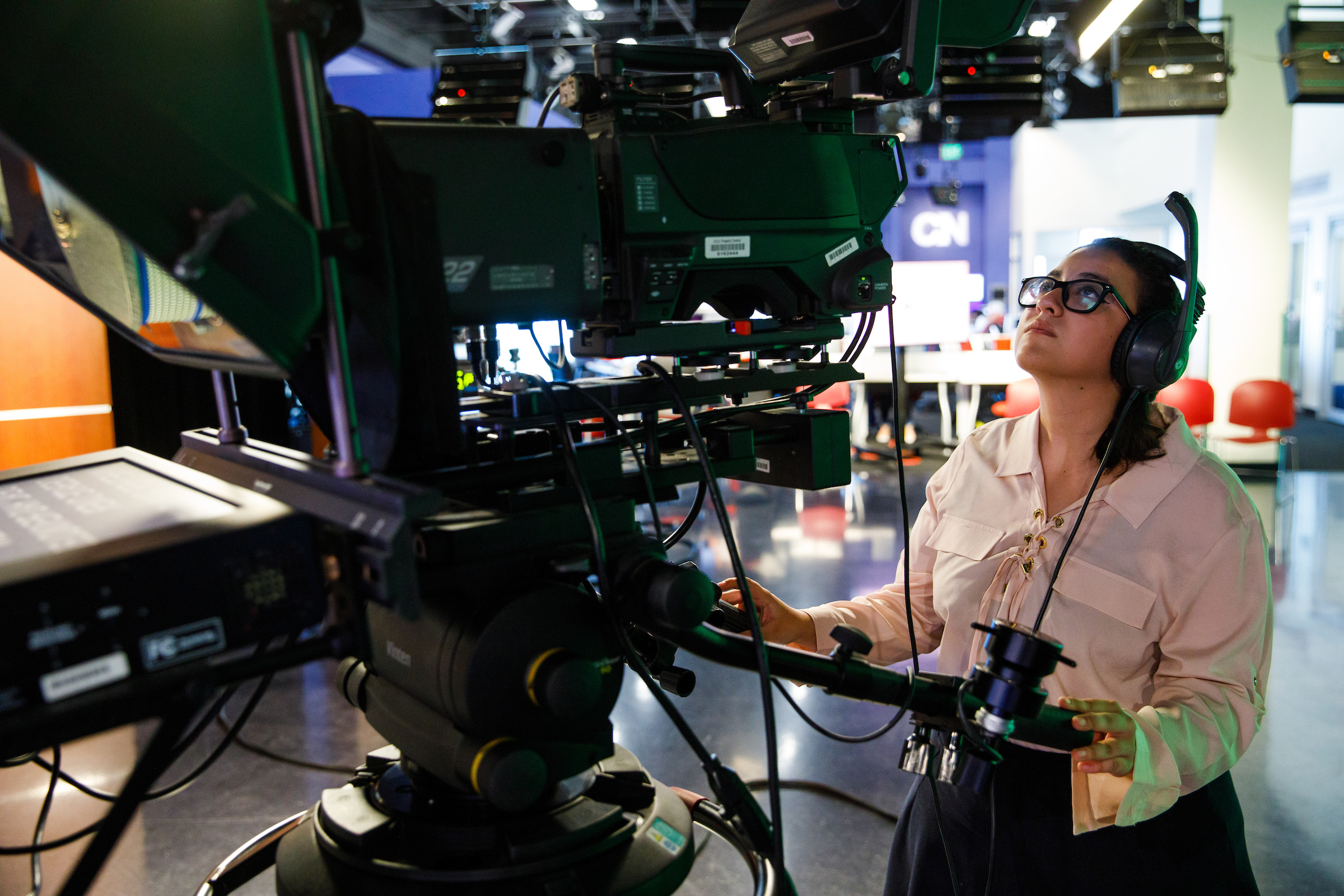 Student journalist stands behind camera in newsroom