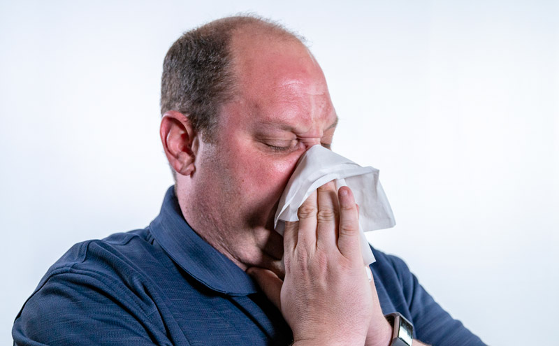 Image of man blowing is nose into tissue. 