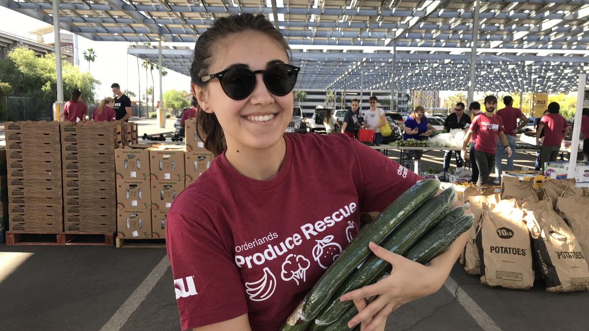 Photo of a person carrying cucumbers and wearing a maroon Borderlands Produce Rescue shirt 