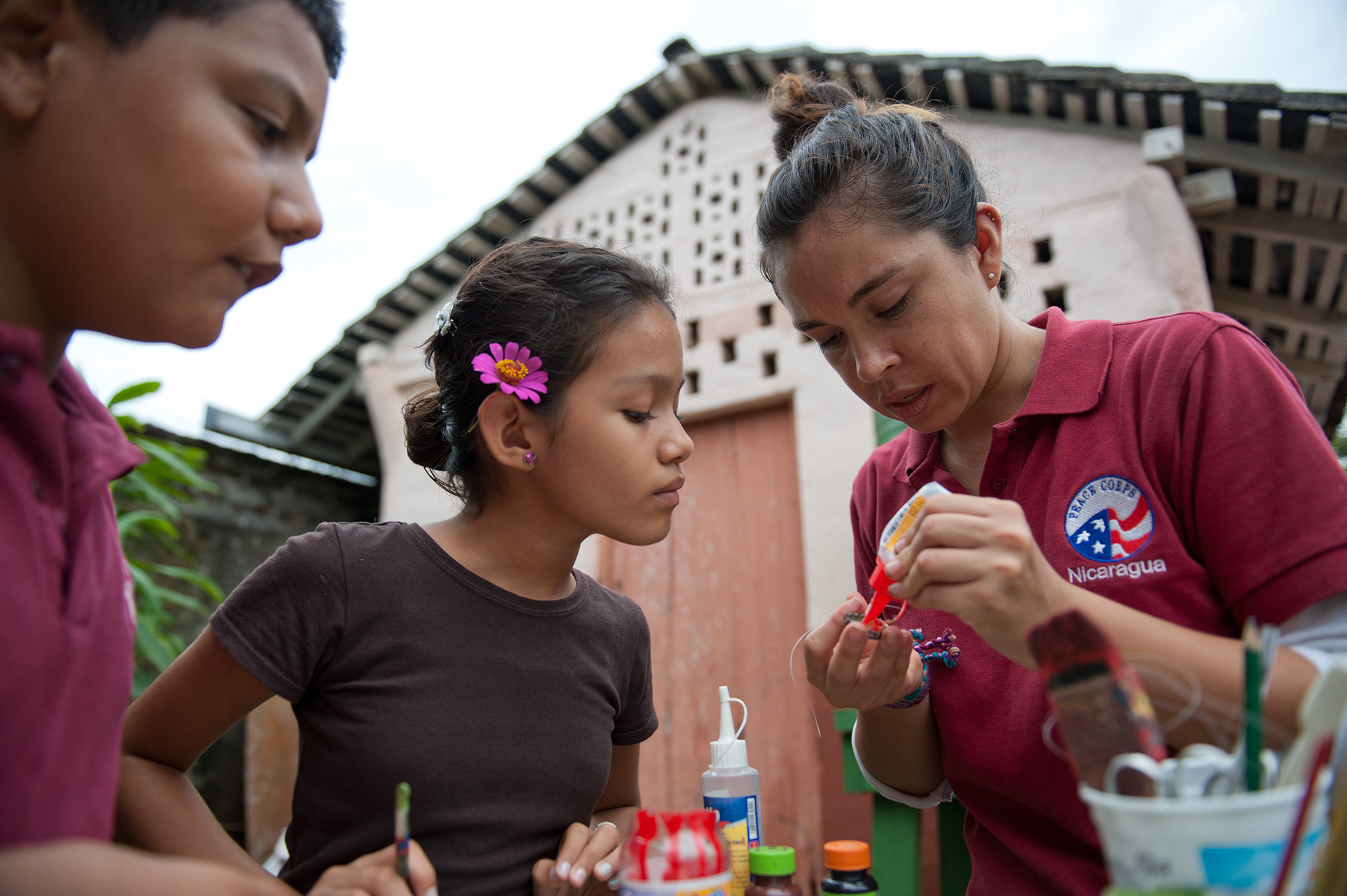 adult Peace Corps member working with two children on crafts