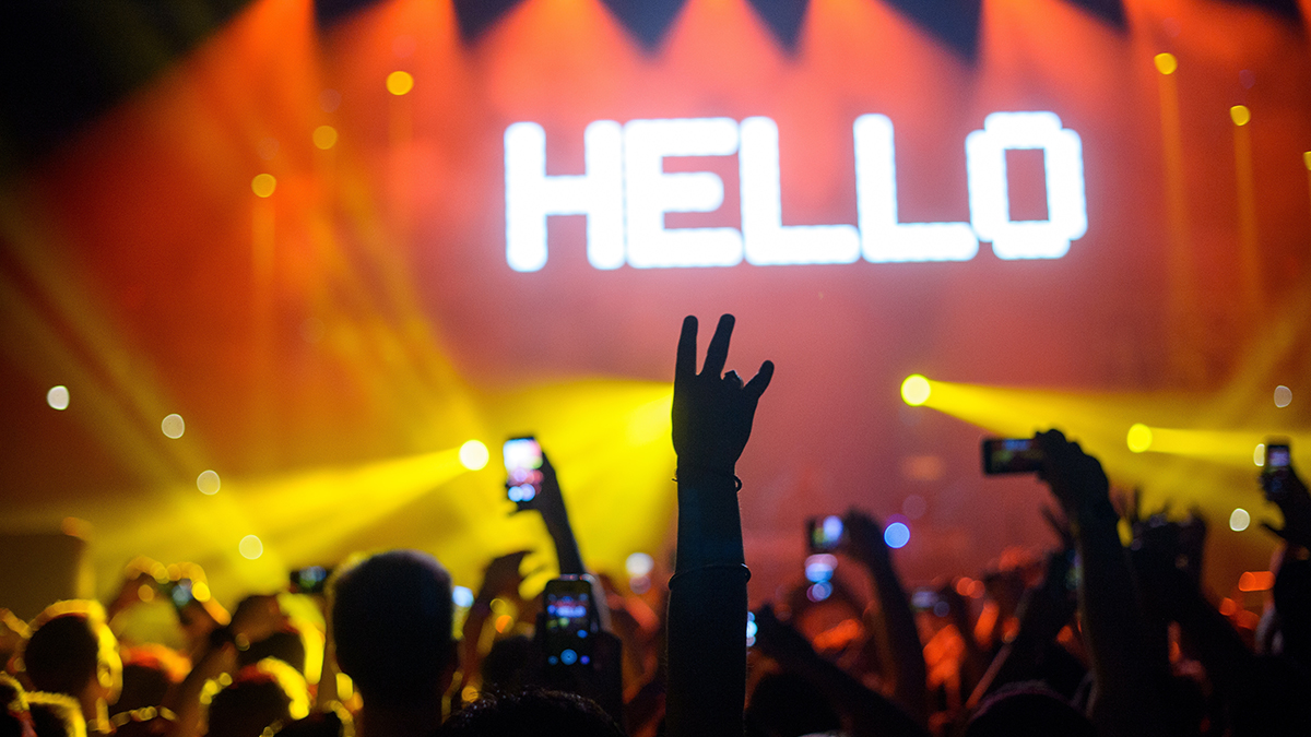 Picture of audience taking smartphone pictures aimed at a concert stage with the word Hello in large, bright white letters.