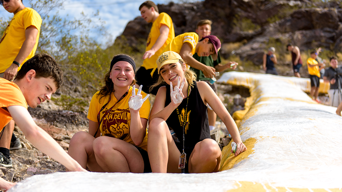 Picture of college students on a mountain painting a large, gold letter A to white.
