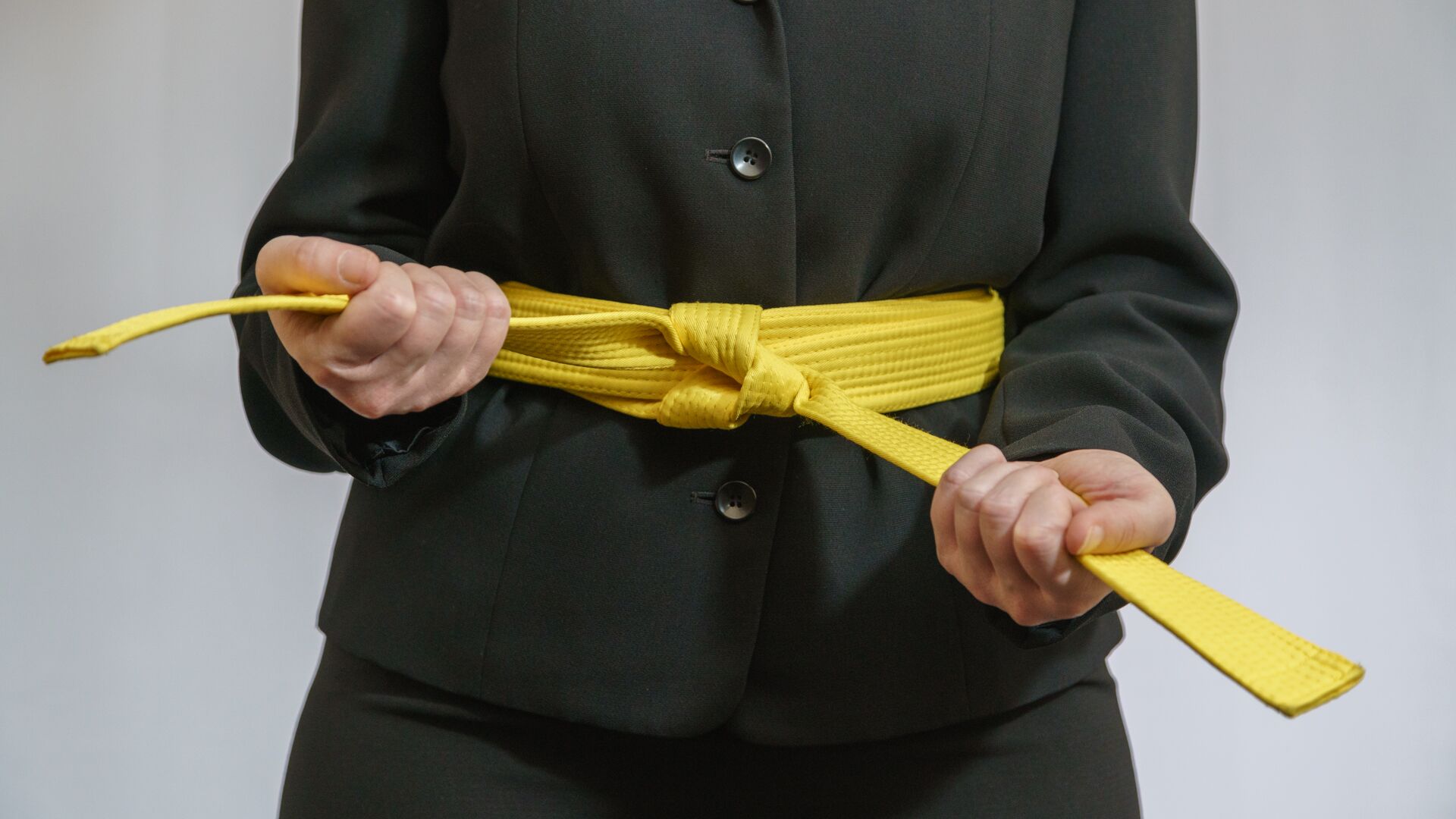 Image of a person in suit tying a yellow belt around waist. 