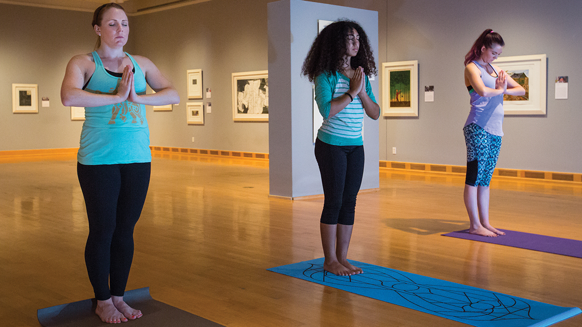Three female students standing side by side in a yoga meditation pose.