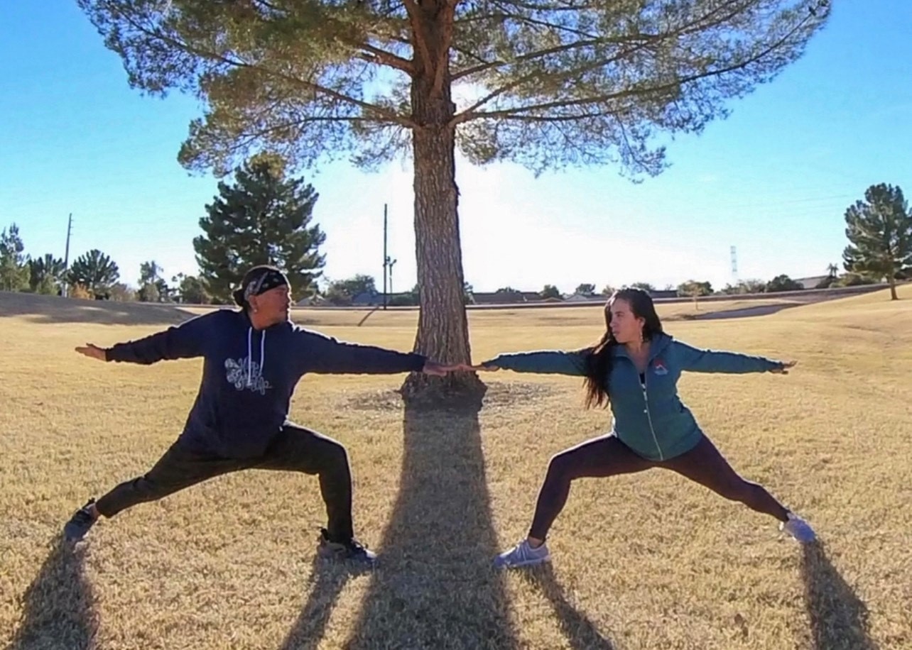 Two people standing stretched in yoga poses with a tree centered between them