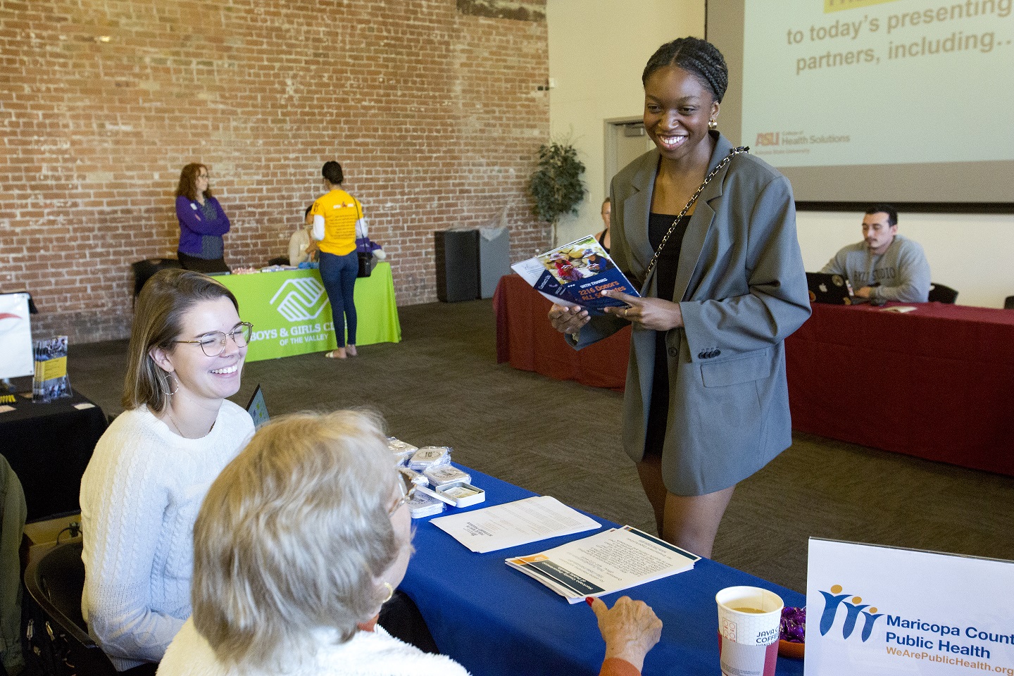 A student smiles and talks with presenters at a table in a large room.