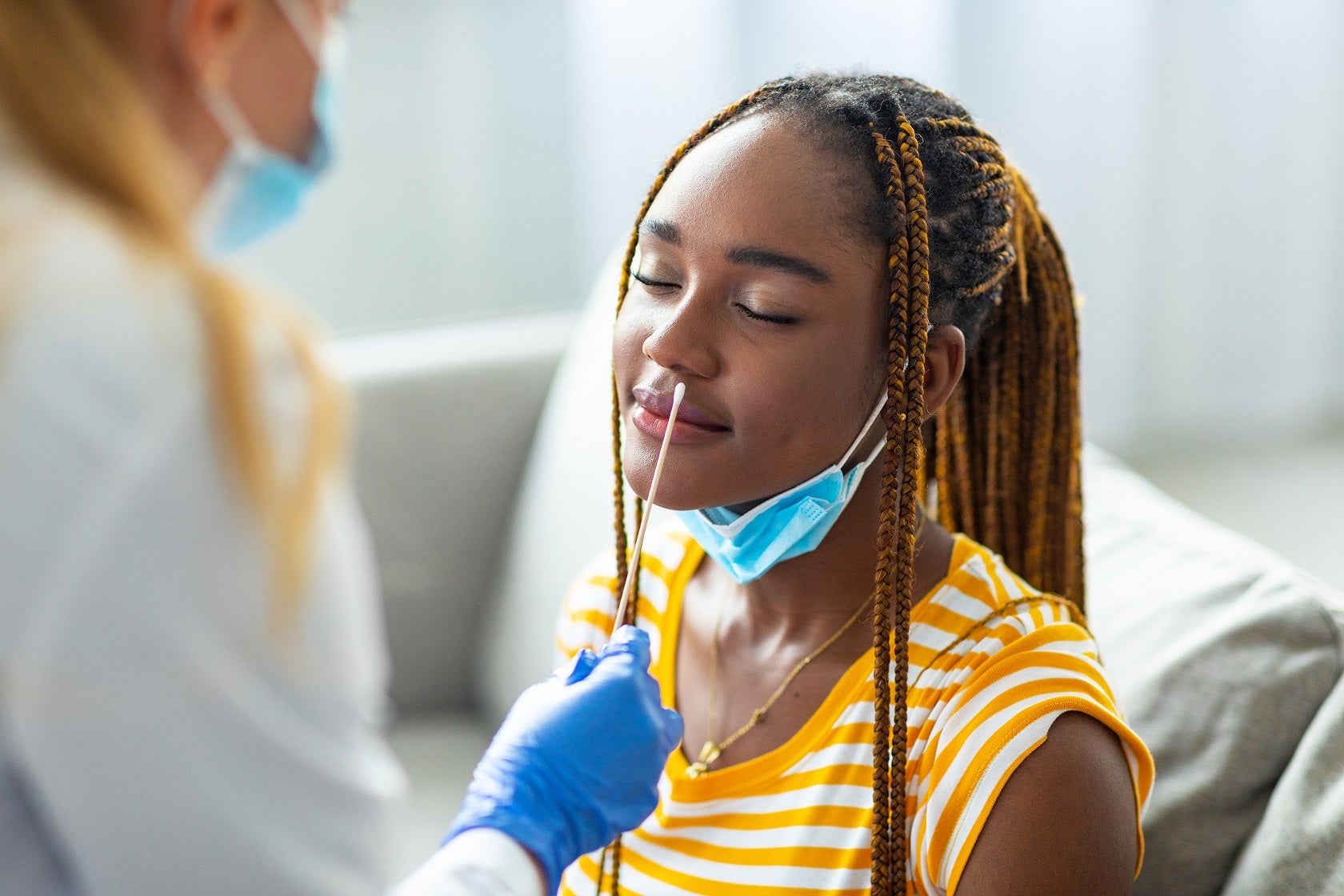 A Black woman in a gold striped shirt sits and waits for a COVID-19 test to be administered