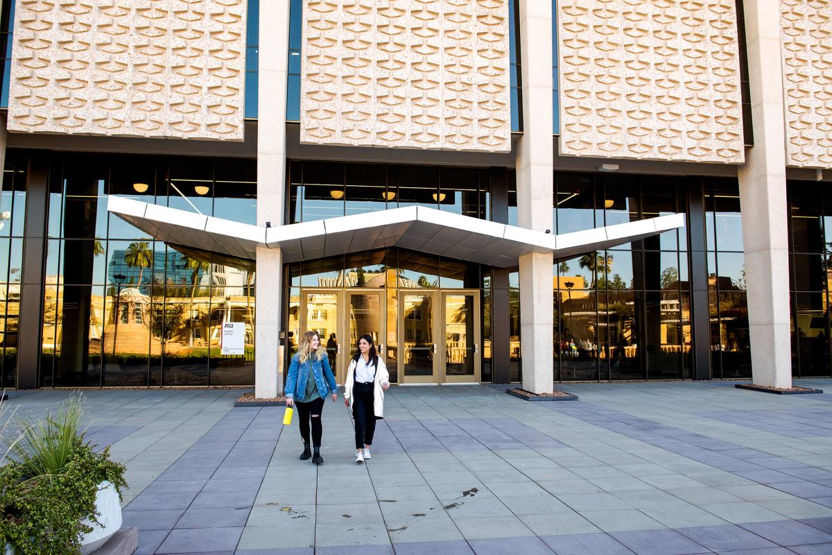 Two people walking outside the exterior of a building