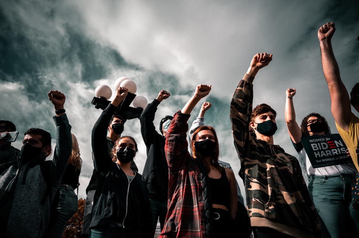 A group of people wearing masks hold their fists up at a protest
