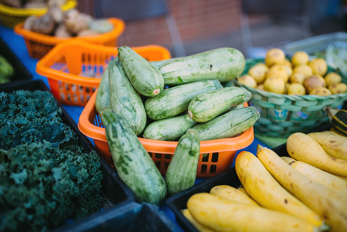 Image of squash in a basket on a table surround by other vegetables. 