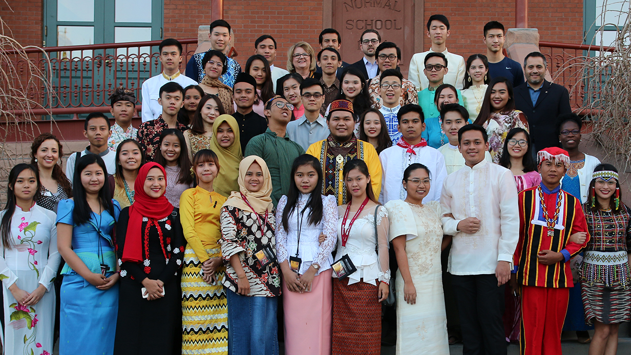 Large group of young adults from all over Southeast Asia wearing clothing representative of their cultures, standing on steps of Old Main in Tempe